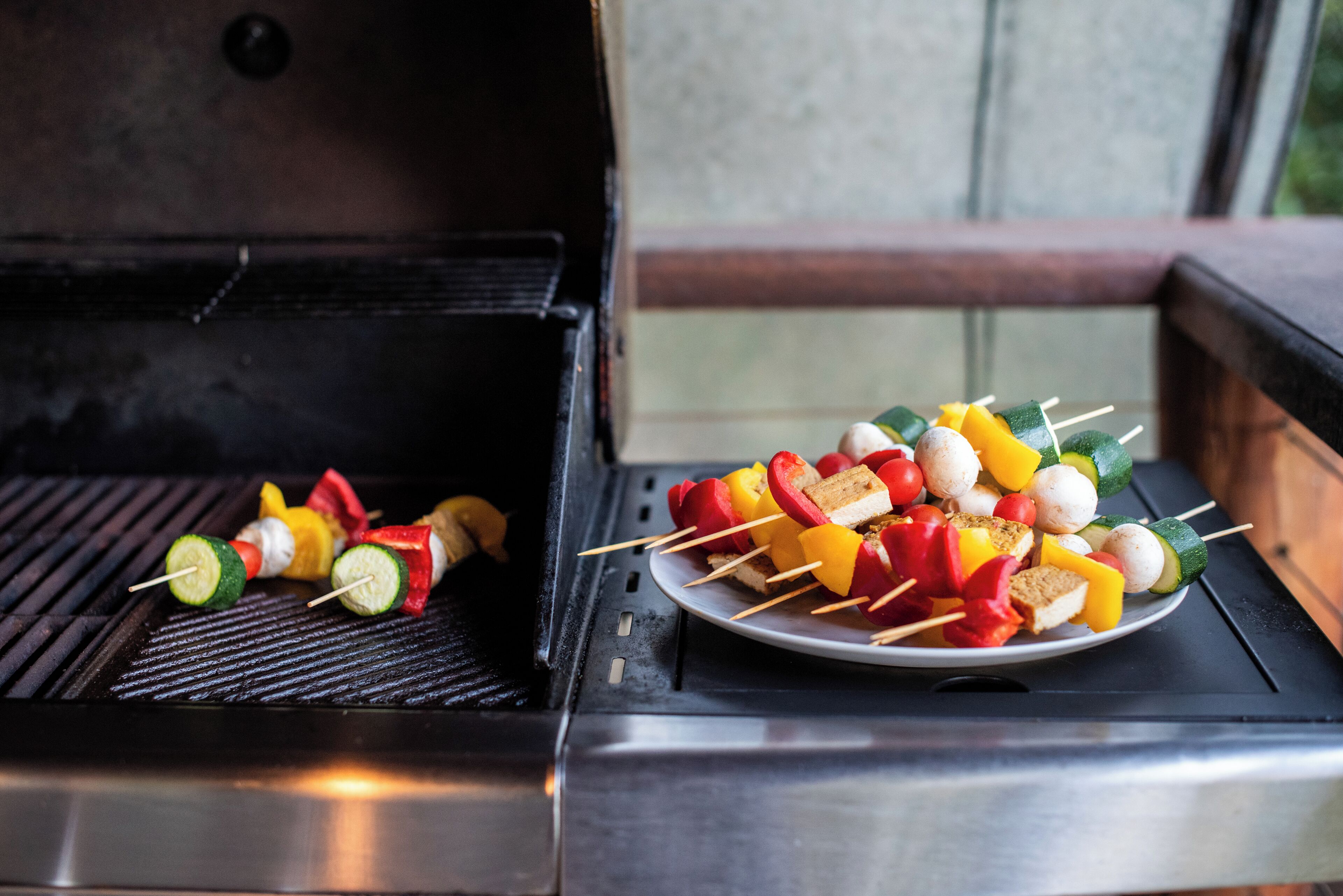 Ein Grill mit Spießen voller Gemüse und Brot, sowie ein Teller mit Spießen daneben.