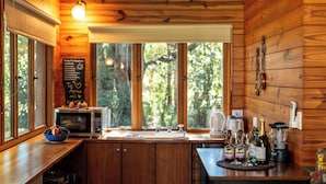 A wooden cabin kitchen with a large window, a microwave, a sink, and various kitchen appliances. -  Kanimbia Cottages (Coolabine)