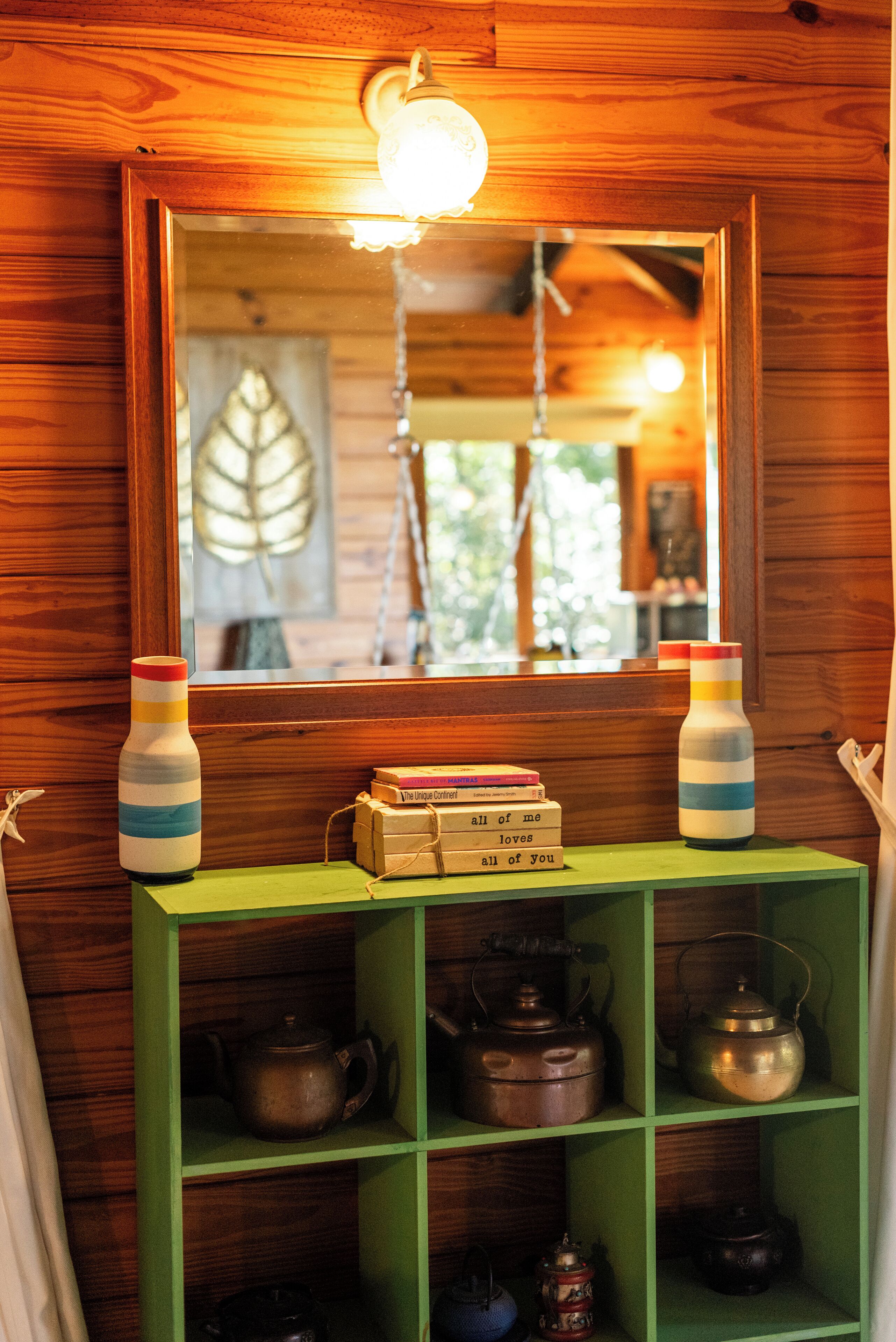 A wooden interior with a mirror reflecting a leaf artwork, two striped bottles, and a shelf with various tea pots.