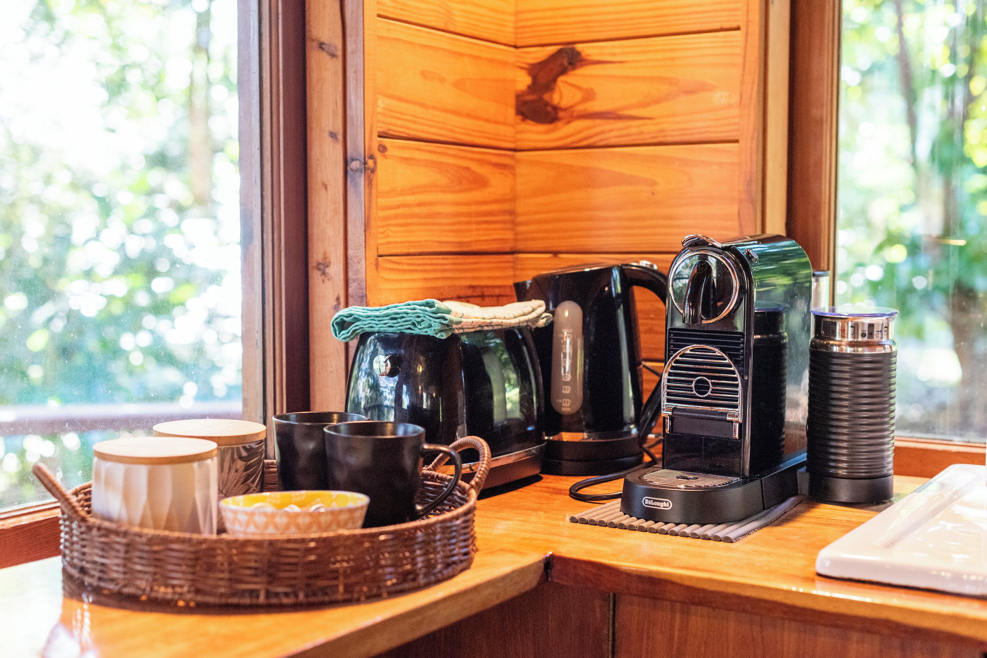 A wooden cabin interior with a coffee station featuring a coffee maker, kettle, and thermos.