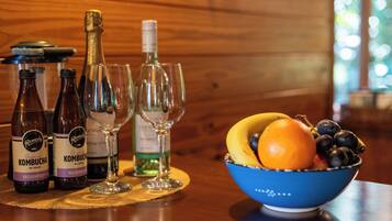 Uma mesa com garrafas de kombucha, uma taça de vinho e uma tigela de frutas.