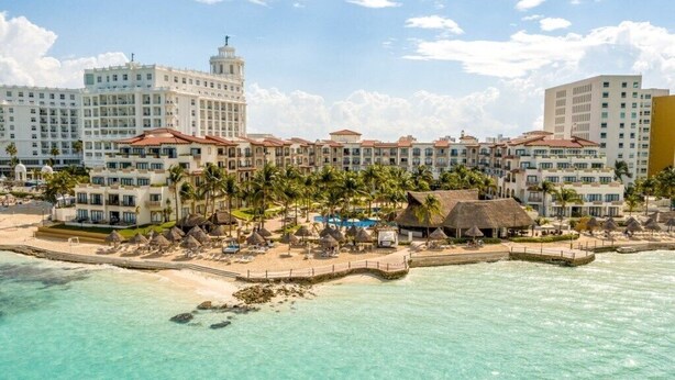 Un hotel frente a la playa con varias edificaciones, un muelle y palmeras.