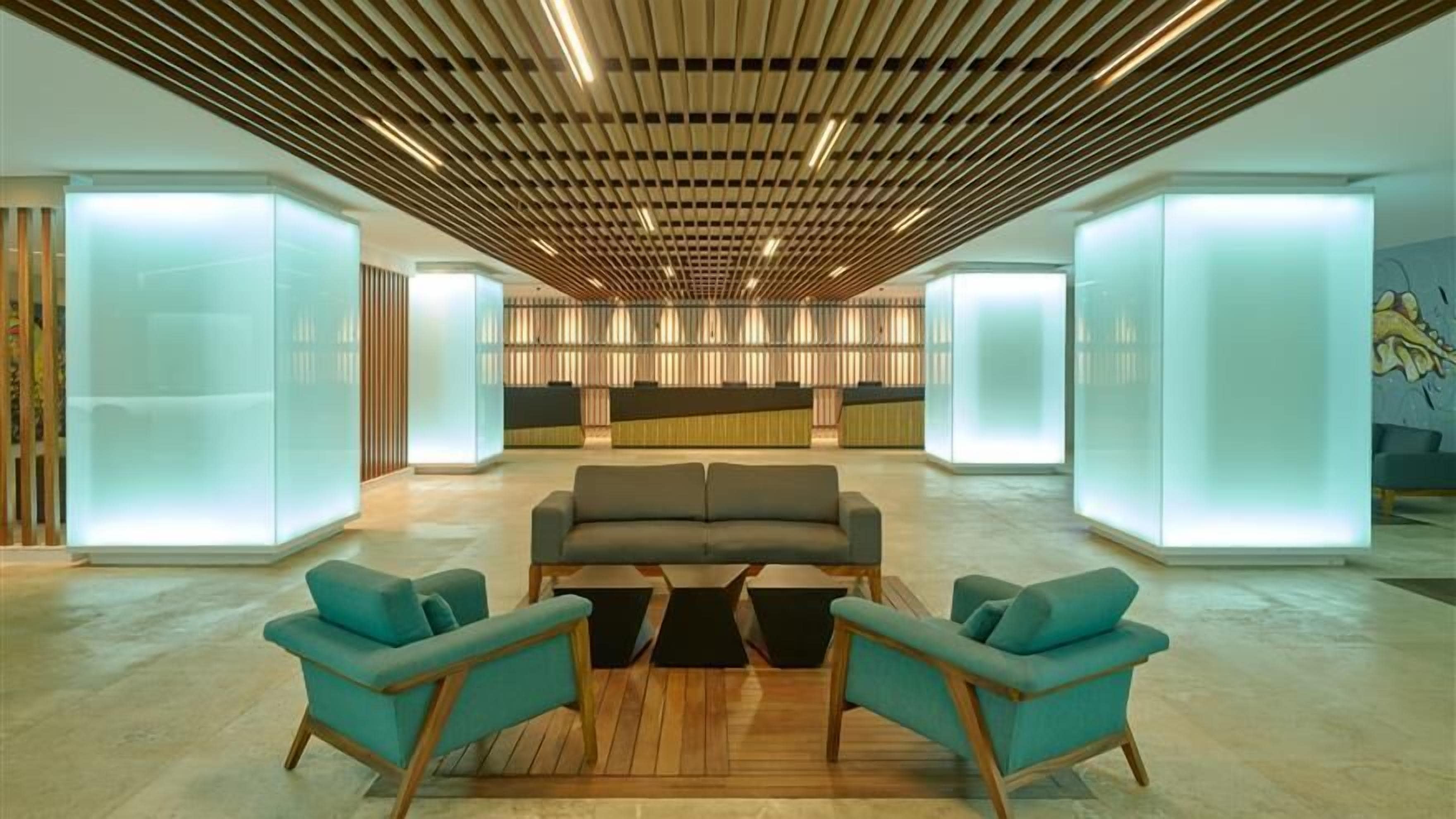 Eine moderne Lobby mit einer zentralen Sitzgruppe, einer Holzdielen-Decke und beleuchteten Glaswänden.