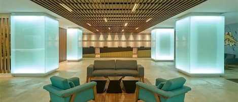 Un vestíbulo moderno con una zona de estar central, techo de listones de madera y separadores de vidrio iluminados.
