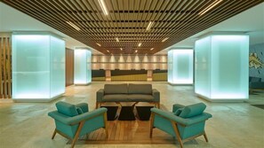 Eine moderne Lobby mit Holzbodenpaneelen an der Decke, einem Empfangstresen und blaugrünen Sesseln.