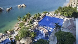 Un resort con una piscina grande, palmeras y vistas a la playa.