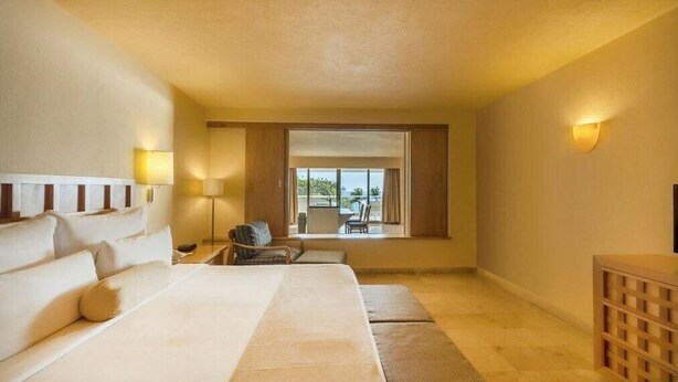 A hotel room with a large bed, a desk, a chair, a TV, and a window with a view.