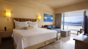 A hotel room with a large bed, a sofa, a TV, and a balcony with a view.