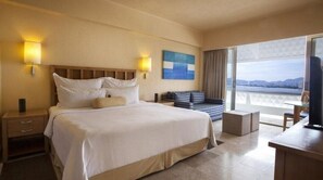 Ein Hotelzimmer mit einem großen Bett, einem Sofa, einem Fernseher und einem Balkon mit Blick.