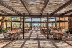 Un'area pranzo all'aperto con tavoli e sedie, una tettoia e palme.