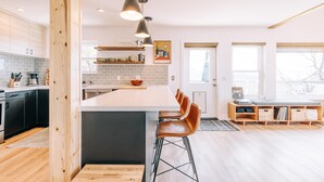 A modern kitchen with a large island, bar stools, and a dining area with a wooden table and chairs. - Escape to Tranquility: Views & Modern Amenities (Idyllwild-Pine Cove)