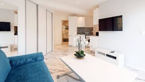 Una cocina moderna con armarios blancos, piso de mármol y un comedor con mesa blanca y sofá azul.