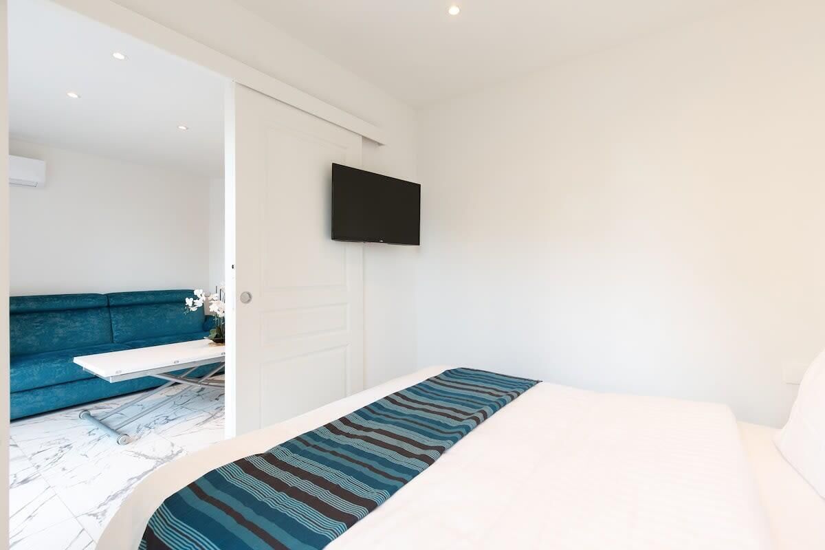 Une chambre à coucher avec un lit, un téléviseur à écran plat fixé au mur, un canapé bleu et une porte blanche.