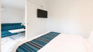 Un dormitorio con una cama, un televisor de pantalla plana montado en la pared, un sofá azul y una puerta blanca.
