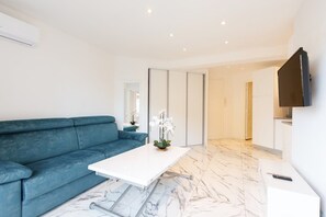 Ein modernes Wohnzimmer mit einem blauen Sofa, einem weißen Couchtisch und einem an der Wand befestigten Flachbildfernseher.