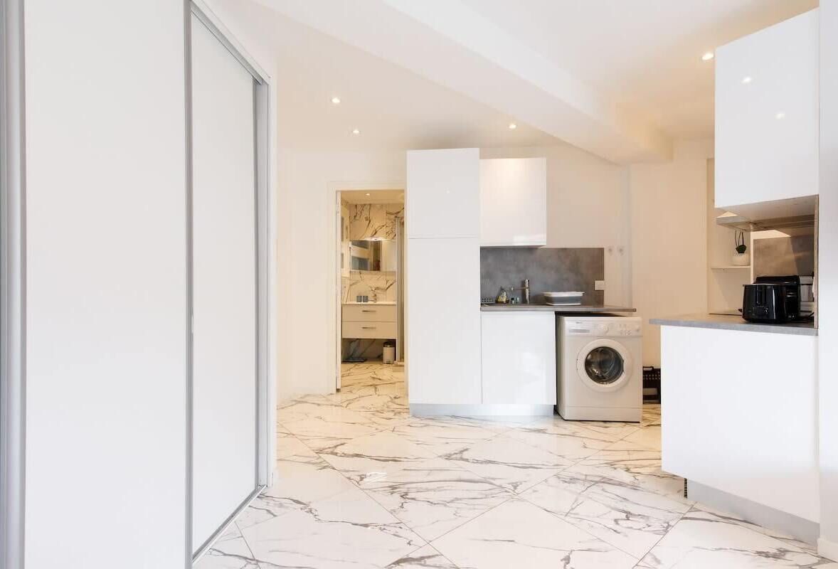 A modern kitchen with a washing machine, marble flooring, and white cabinetry.