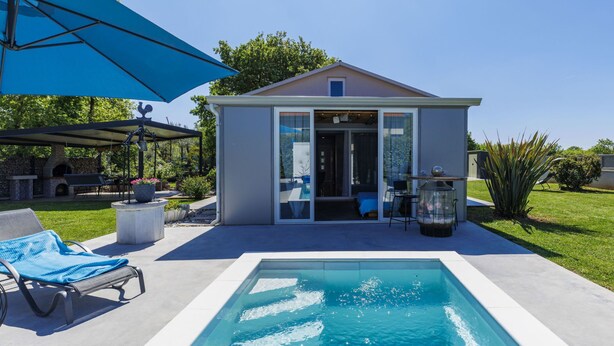 A swimming pool with a patio area, a covered seating area, and a small building with a glass door.