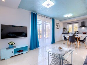 Ein modernes Wohnzimmer mit Fernseher, einem Essbereich mit Tisch und Stühlen sowie einer Küche mit Herd.
