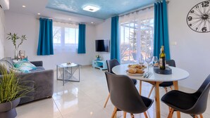 A modern living room with a grey sofa, a glass coffee table, and a dining area with a round table and chairs.