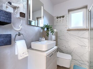 Ein modernes Badezimmer mit einem weißen Waschbecken, einem Handtuchhalter, einem Spiegel, einer Pflanze und einer Toilette.