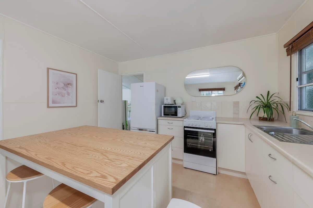 Een kleine keuken met een houten tafel, witte kastjes, een magnetron, een oven en een spoelbak.