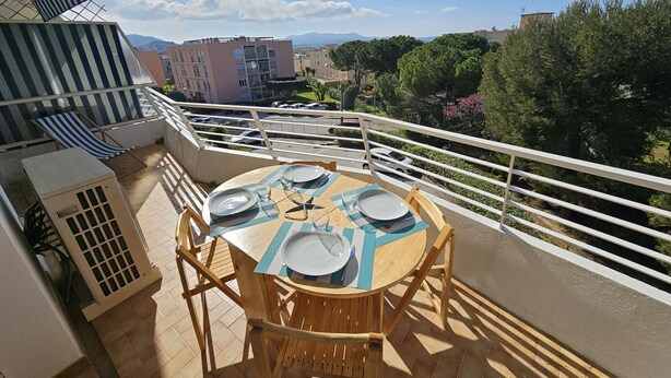 Ein Balkon mit einem runden Holztisch, gedecktem Platz für vier Personen, einem gestreiften Stuhl und einem weißen Geländer.