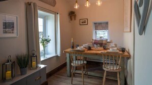 Un comedor con una mesa de madera dispuesta para dos, una ventana con cortinas y una lámpara fijada a la pared.