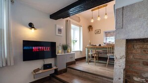 Una sala de estar moderna con una televisión de pantalla plana, piso de madera, chimenea y un comedor con mesa y sillas.