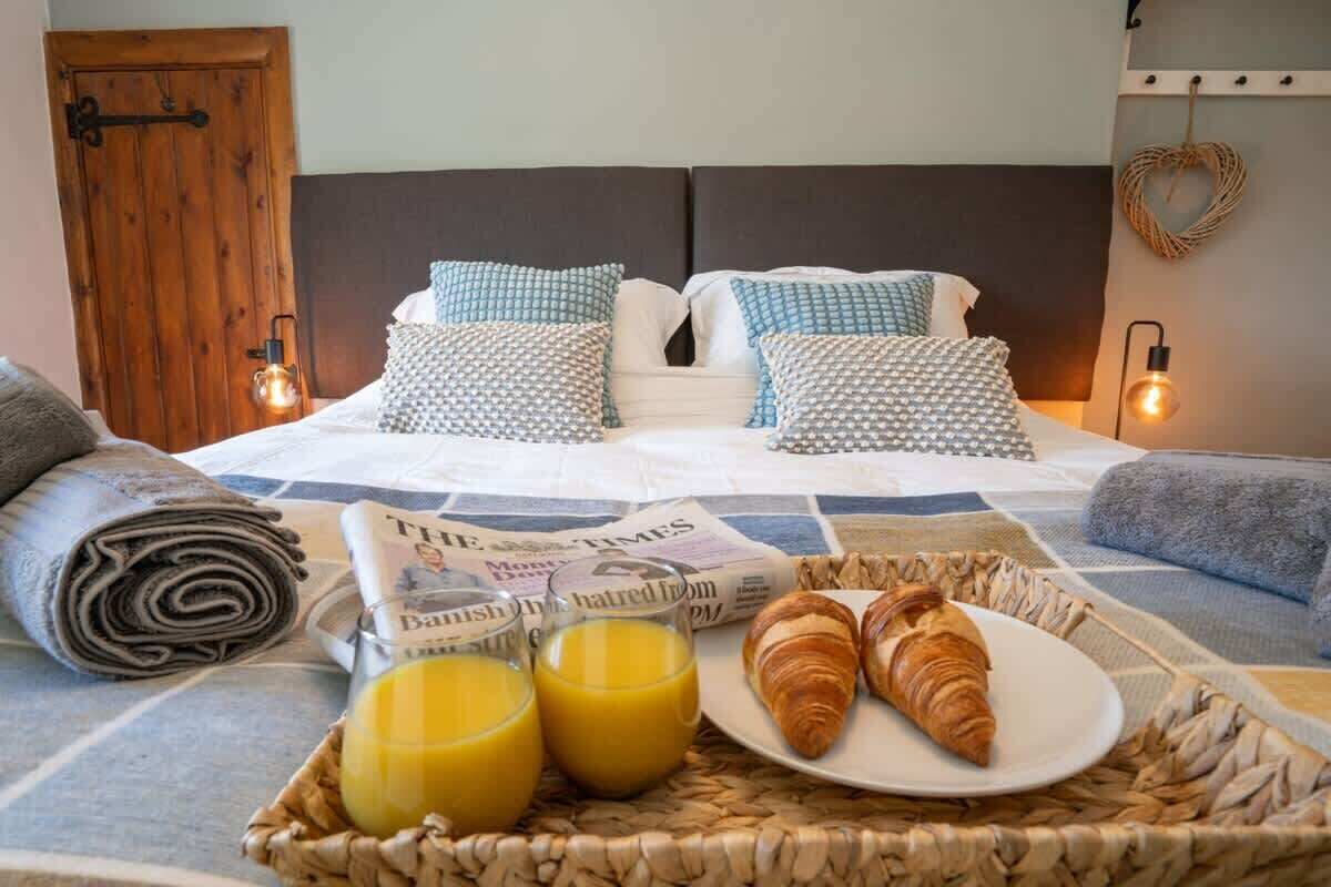 A neatly made bed with patterned pillows, a breakfast tray with croissants and orange juice, and a newspaper.