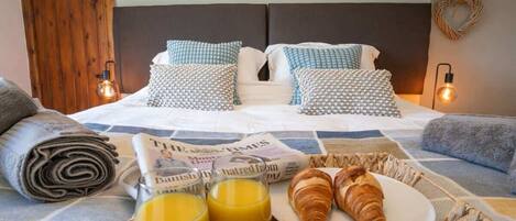 A neatly made bed with patterned pillows, a breakfast tray with croissants and orange juice, and a newspaper.