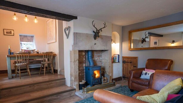 Una sala de estar acogedora con chimenea de piedra, un sillón de cuero y un comedor con sillas de madera.