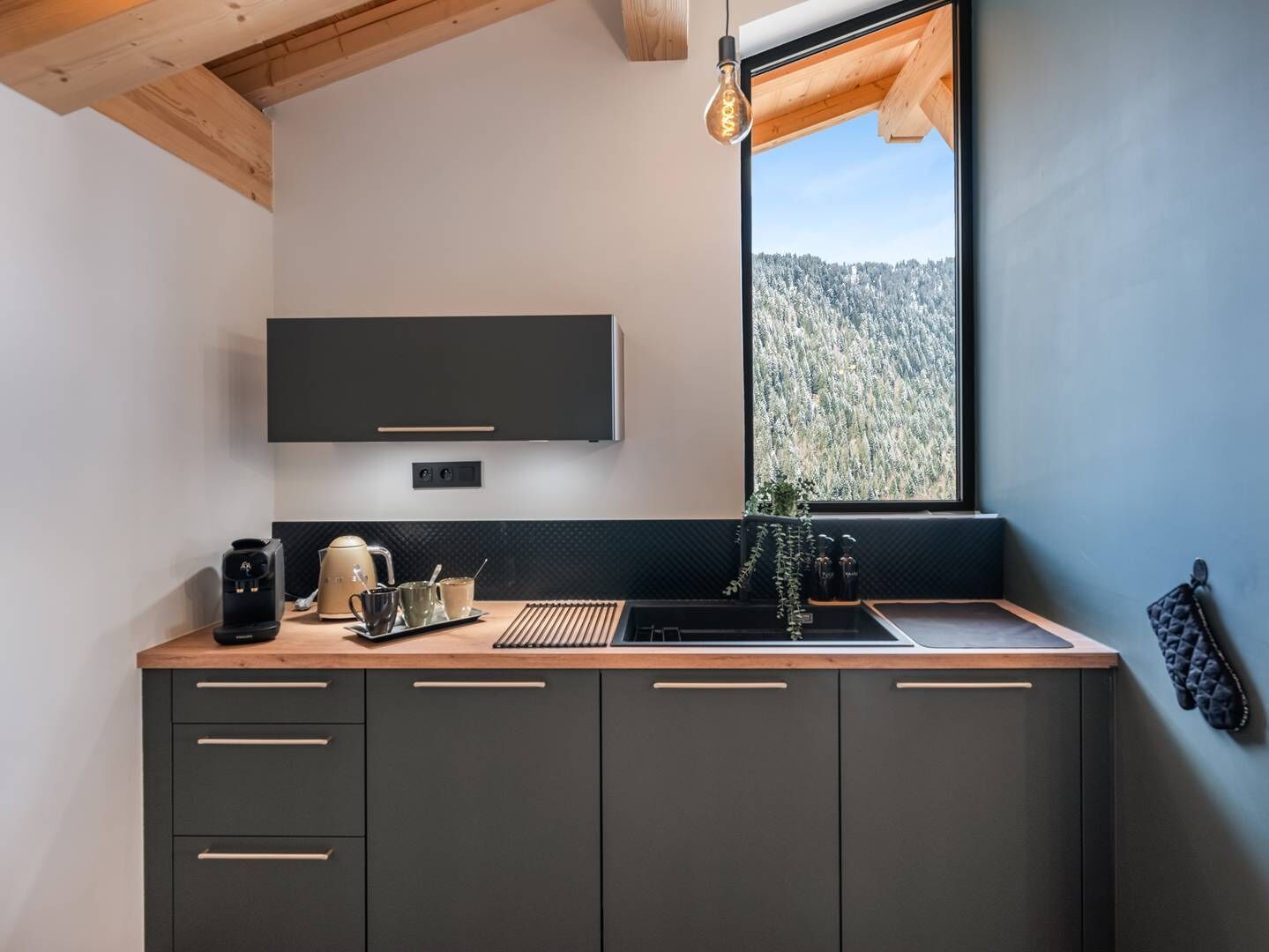 A modern kitchen with a built-in stove, a sink, and a window with a view of a forest.