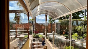 A glass-walled staircase leading to a covered outdoor area with a view of a garden and a building with a red-tiled roof. - Hacienda Hotel Los Caballeros  (Marinilla)