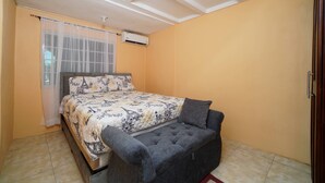 Ein Schlafzimmer mit Bett, einer Sitzbank, einer Klimaanlage und einem Fenster mit Vorhängen.