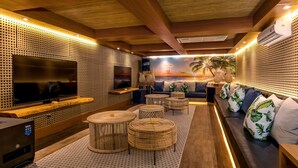 Una sala de estar moderna con un televisor de pantalla plana grande, asientos cómodos y un mural en la pared con un atardecer sobre el océano.