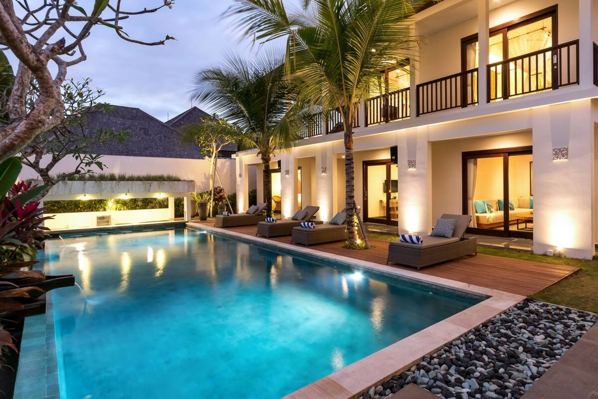 A modern hotel with a swimming pool, outdoor seating, and a well-lit balcony.