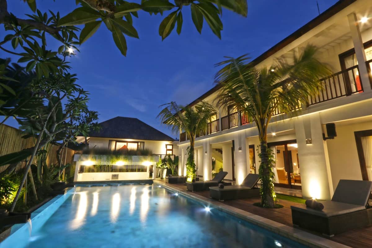 A modern resort with a swimming pool, lounge chairs, and a well-lit building.