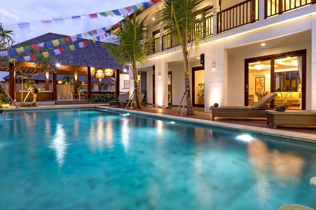 A swimming pool with lounge chairs and a covered area with flags.