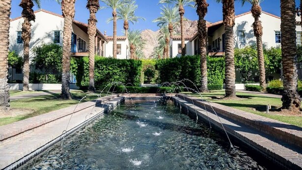 Un patio con fuente de agua, palmeras y edificios de estilo arquitectónico mediterráneo.