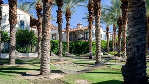A courtyard with palm trees, a hammock, and a building with a tiled roof. - Luxury Resort Villa w/Pool, Hot Tubs & Views (La Quinta)