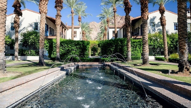 A courtyard with a central water feature, surrounded by palm trees and buildings with a Mediterranean architectural style. - Luxury Resort Villa w/Pool, Hot Tubs & Views (La Quinta)