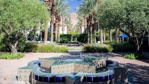 A courtyard with a tiled fountain, palm trees, and a building in the background.