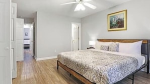 A bedroom with a bed, a ceiling fan, a nightstand, and a painting on the wall.