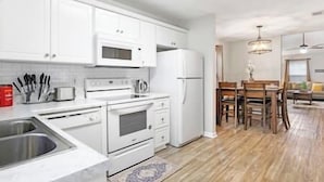 A modern kitchen with white cabinets, a stainless steel sink, and a dining area with wooden chairs and a chandelier.