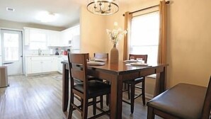 A dining area with a wooden table and chairs, a vase with flowers, and a window with curtains.