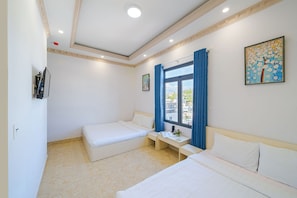 A hotel room with two beds, a desk, a window with blue curtains, and a painting on the wall. - RAON Central Hotel (Xuan Huong - Da Lat)