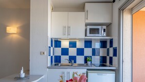 A compact kitchen with white cabinets, a microwave, and blue and white checkered backsplash. - Primavera by Interhome (Cap d'Agde)