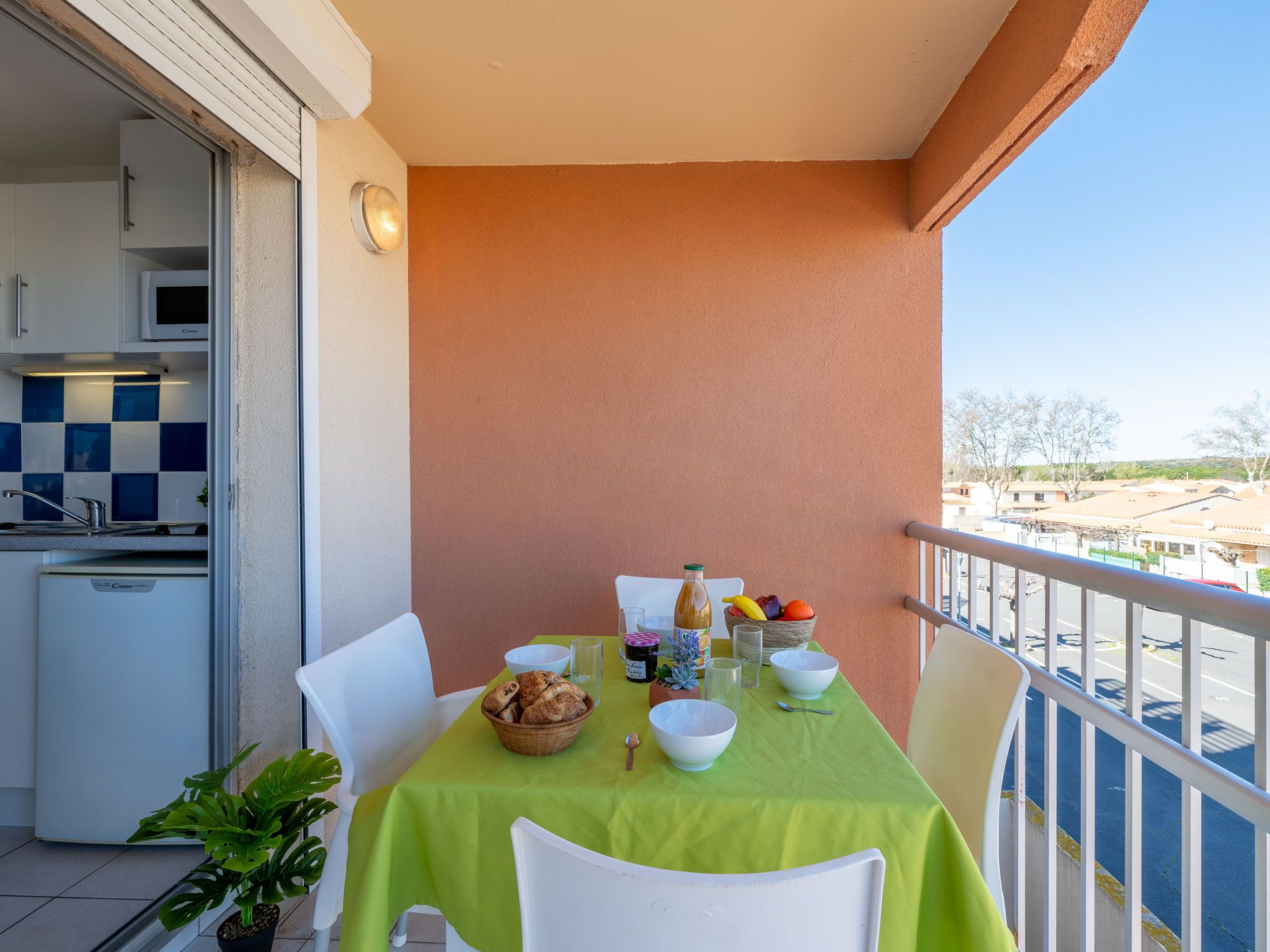 A balcony with a table set for two, a small kitchen area, and a view of the street.
