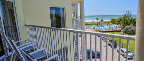 Un balcon avec des chaises blanches, donnant sur une piscine et une plage.