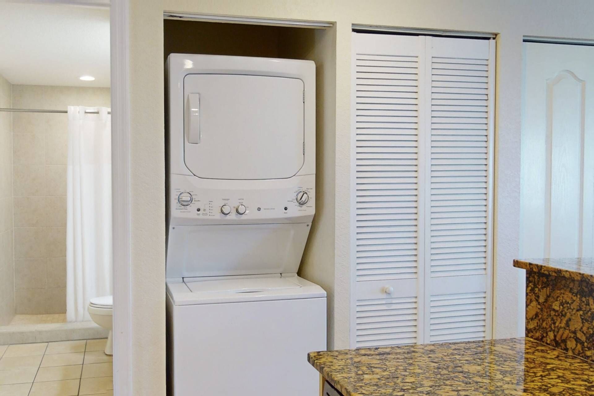 A laundry room with a washer and dryer, a shower, and a door with louvered panels.